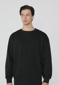 Zwarte sweatshirt met een losse pasvorm, gemaakt van zacht materiaal, met een ronde hals, verlaagde schouders en ribgebreide manchetten. Minimalistisch ontwerp.