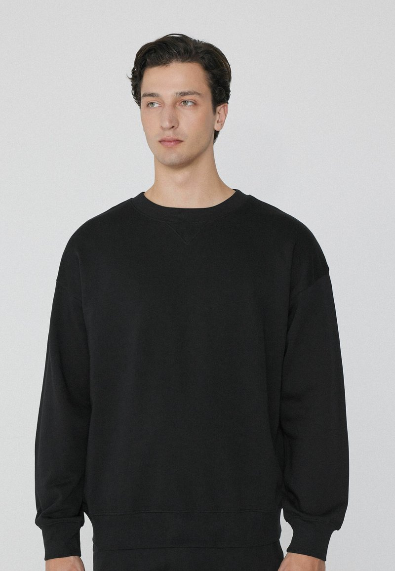 Zwarte sweatshirt met een losse pasvorm, gemaakt van zacht materiaal, met een ronde hals, verlaagde schouders en ribgebreide manchetten. Minimalistisch ontwerp.