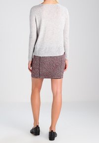 Pull en tricot gris clair à manches longues, associé à une jupe à motifs rouges et noirs. Des chaussures noires complètent la tenue.