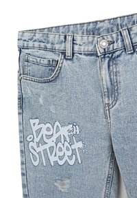 Jeans in denim azzurro chiaro con toppe strappate e testo in stile graffiti bianco che recita "Beat Street" sul davanti.