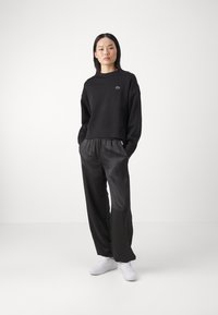 Musta puuvillainen printtipaita, jossa on pyöreä kaula-aukko ja brodattu logo, yhdistettynä löysiin, kiiltäviin mustiin satiinipö trousers ja valkoisiin lenkkareihin.