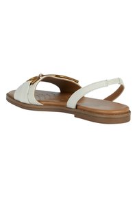 Vita läder platt sandal med öppen tå, guldspänne detaljer och en tunn rem runt hälen på en brun sula.