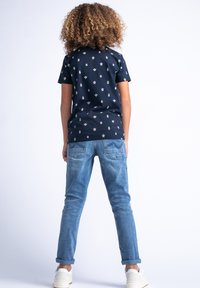 Camiseta de manga corta en azul marino con estampados de estrellas multicolores y latas, combinada con jeans ajustados de color azul claro y zapatillas blancas.