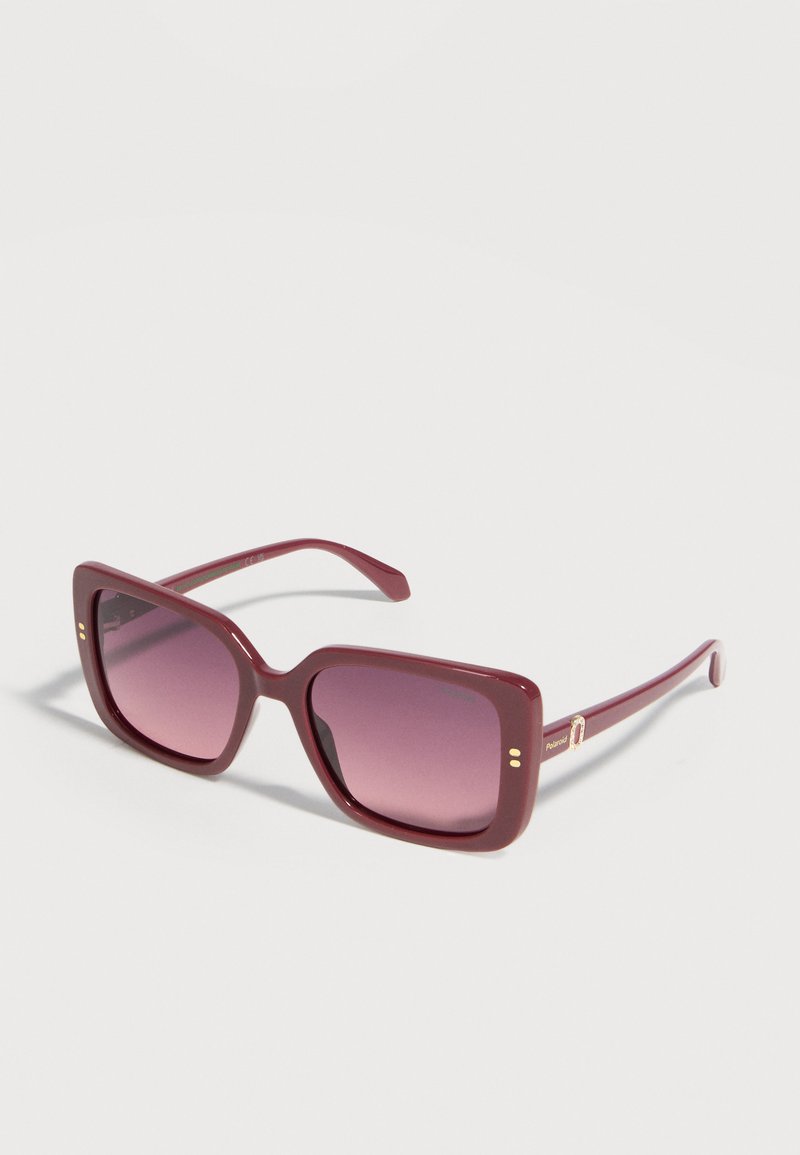 Lunettes de soleil carrées bordeaux avec verres dégradés violets et accents dorés subtils sur les branches, présentées sur un fond blanc.