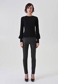 Schwarzes Strickoberteil mit strukturierten, gepufften Ärmeln, kombiniert mit engen schwarzen Lederhosen und schwarzen High Heels. Einfaches und elegantes Design.