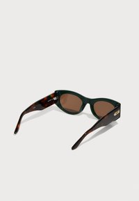 Ochelari de soare tortoise verzi cu un design cat-eye, lentile maro și accente subtile din aur pe tâmple.
