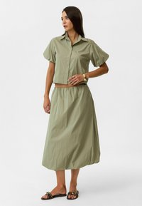 Olijfgroene twee-delige set met een cropped button-up shirt met puffende korte mouwen en een bijpassende hoge taille rok met een elastische tailleband.