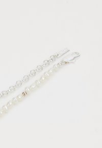 Bracciale in argento con catena, caratterizzato da perle bianche irregolari, chiusura a moschettone e un piccolo tag inciso. Texture liscia con finitura lucida.