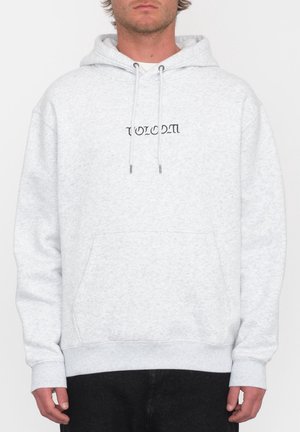 Man draagt een lichtgrijze hoodie met een voorzak en zwarte gestileerde tekst "Volcom" in het midden van de borst.