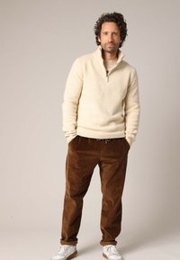 Crème zip-up sweater met geribbelde manchetten, gecombineerd met bruine corduroy broek en witte sneakers. Zachte textuur en ontspannen pasvorm.