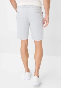 Pantaloni corti grigio chiaro realizzati in un tessuto morbido, con un design classico, tasche laterali e posteriori, e una cintura comoda. Indossati con scarpe bianche.