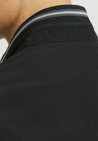 Fekete dzseki gallér sima textúrával, vékony fekete, szürke és fehér csíkokkal. Minimális dizájn, letisztult varratok.