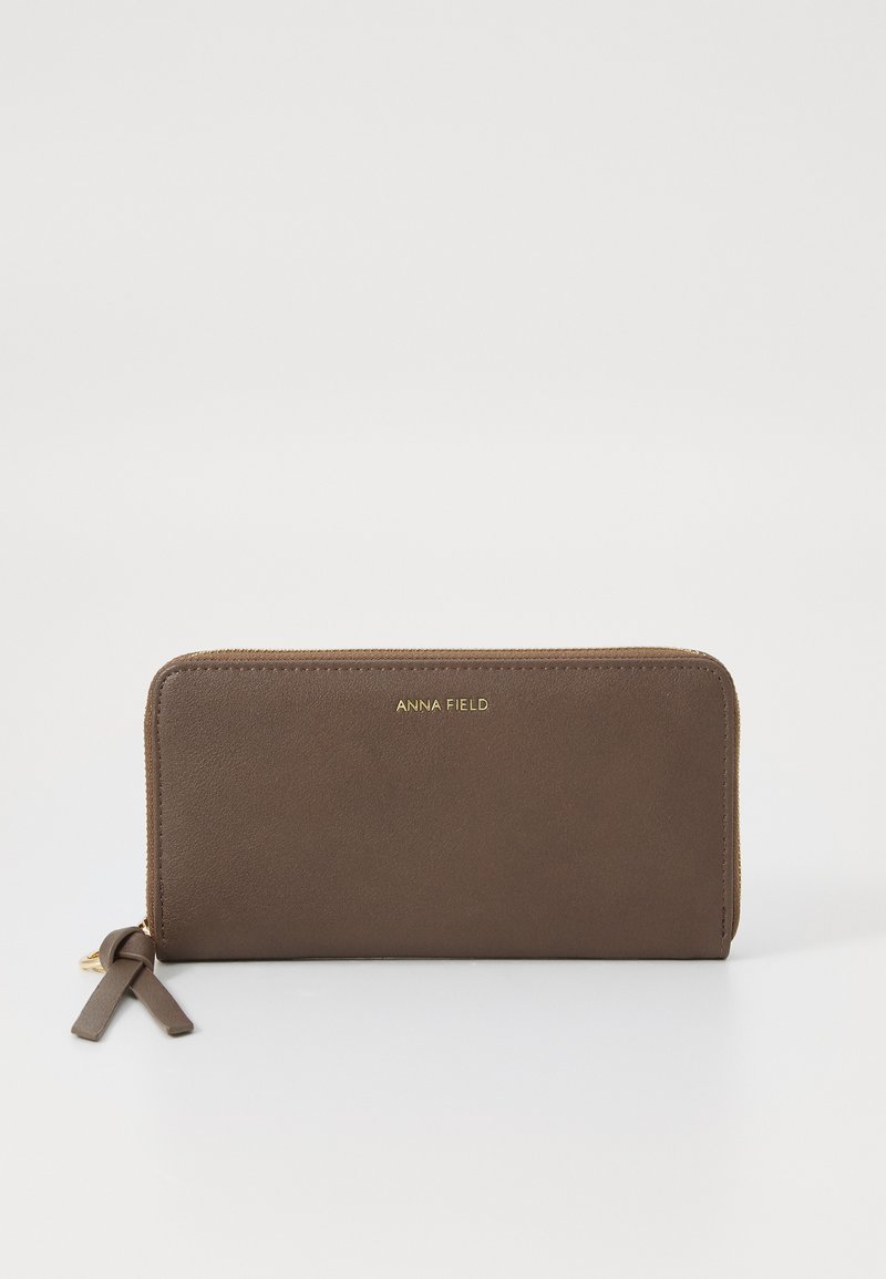 Brunt læderpung med et elegant design, gyldent logo, lynlåslukning og en dekorativ kvast. Glat tekstur og rektangulær form.