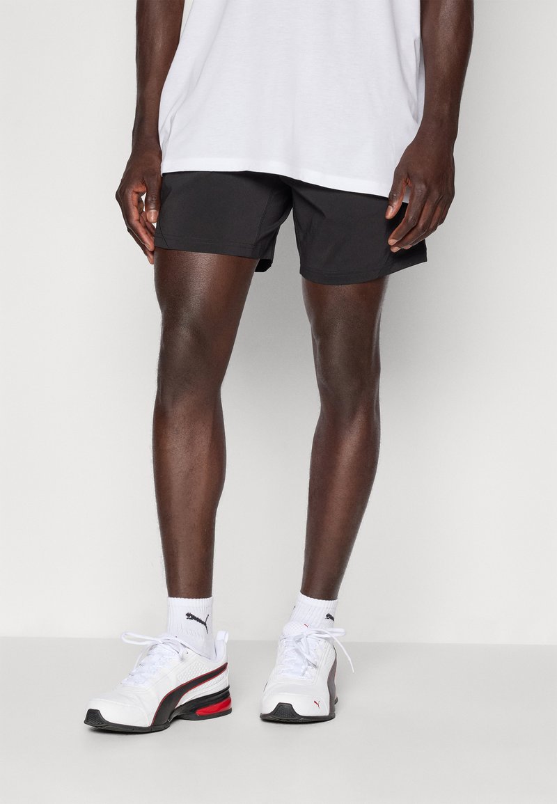 Zwarte sportshorts, witte sneakers met rode accenten en witte sokken. Eenvoudig ontwerp, lichtgewicht materiaal en een aansluitende snit.
