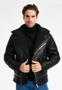 Czarna kurtka z owczej wełny z szerokim kołnierzem, zamkami błyskawicznymi i bocznymi kieszeniami. Posiada gładką skórę oraz teksturowaną podszewkę.