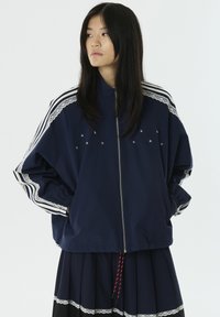 Marineblauwe bomberjack met witte gestreepte accenten en kantafwerking, voorzien van geborduurde sterren en een volledige ritssluiting. Ontspannen pasvorm.