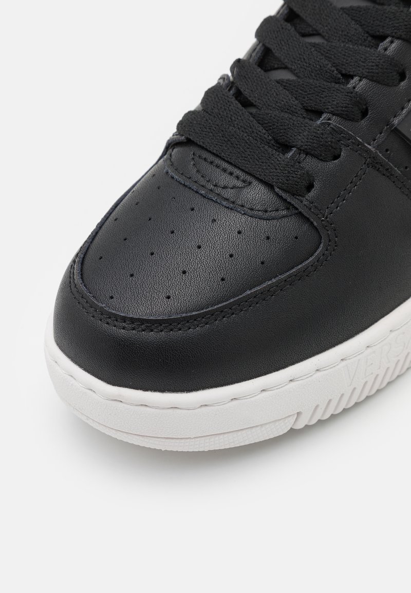 Sneaker in pelle nera con punta perforata, lacci neri piatti e suola in gomma bianca. Presenta dettagli testurizzati sulla parte superiore e marchio laterale.