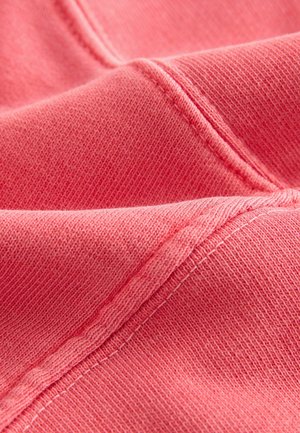 Korallroza audums ar mīkstu tekstūru, ar redzamām šuvēm un heatherēta dizaina rakstu. Materiāls izskatās viegls un elastīgs.