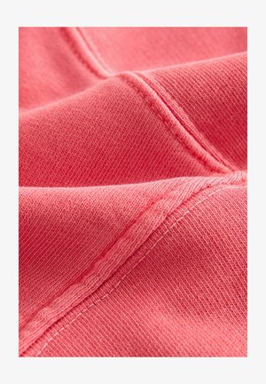 Korallroza audums ar mīkstu tekstūru, ar redzamām šuvēm un heatherēta dizaina rakstu. Materiāls izskatās viegls un elastīgs.