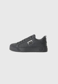 Black sneakers with textured material, flat sole, round toe, and laces; includes a rectangular brand tag on the side.