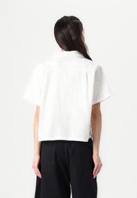 White short-sleeve top with a textured pattern, collared neckline, and a cropped cut, paired with black wide-leg pants.