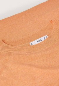 Morbido maglione arancione con un collo lavorato a maglia rotondo, dotato di un'etichetta cucita all'interno. Il materiale presenta una leggera texture e una sottile variazione di tonalità.