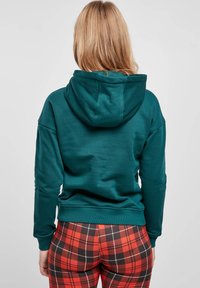 Teal huppari, jossa on pehmeä rakenne, suurella hupulla ja laskevilla olkapääsaumoilla, yhdistettynä punamustiin ruutuhousuihin.