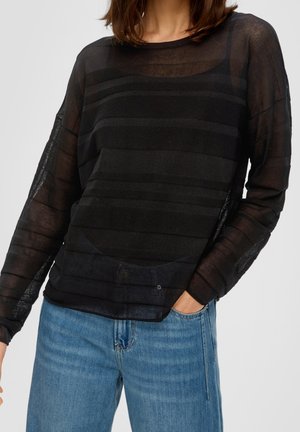 Haut long à manches transparentes de couleur noire avec un design à rayures transparentes, col rond et coupe loose. Associe à un jean en denim bleu clair.