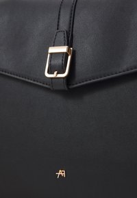 Schwarze Lederhandtasche mit einer goldenen Schnalle an der Klappenverschlus und einem kleinen geprägten Logo am Boden. Glatte Textur, strukturiertes Design.