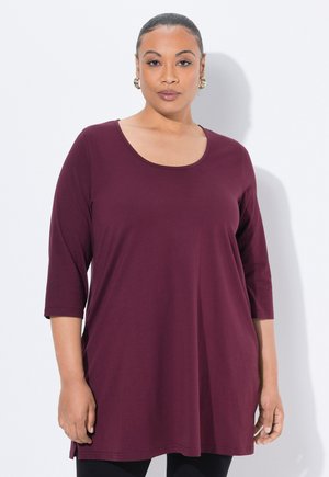 Tunika bordeaux realizzata in tessuto morbido, con maniche a tre quarti e scollatura tonda, dal fit rilassato, abbinata a leggins neri.