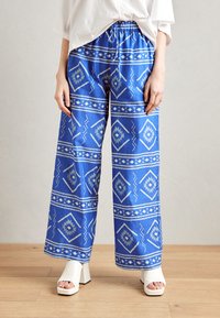 Pantalons larges à motifs bleus avec des designs géom�étriques blancs. Taille ajustable avec cordon de serrage, tissu léger et coupe décontractée.