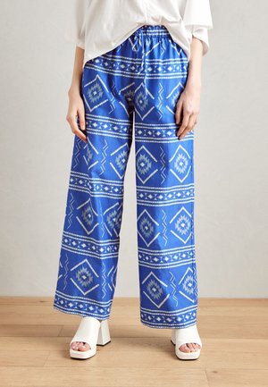 Pantalons larges à motifs bleus avec des designs géométriques blancs. Taille ajustable avec cordon de serrage, tissu léger et coupe décontractée.