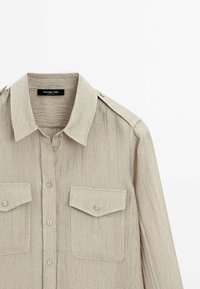 Chemise beige texturée à manches longues avec devant boutonné, deux poches poitrine à rabat et épaulettes, étiquetée Massimo Dutti.