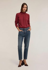 Blusa roja con cuello de volantes, vaqueros de tiro alto azul y zapatos de tacón cuadrado burdeos. Tela suave y corte relajado.