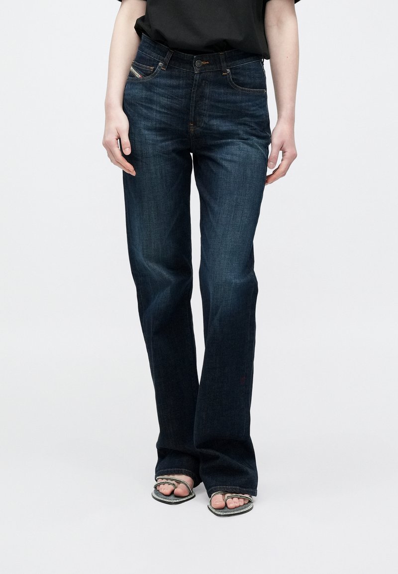 Σκούρα μπλε τζιν με φαρδιά καμπάνα από τζιν υλικό, με το κλασικό σχέδιο πέντε τσεπών, εμφανείς ραφές και ελαφριά σκιάσεις στο εμπρός μέρος.