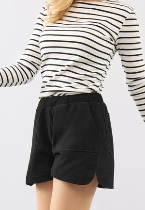 Kvinde iført sorte elastiske shorts med store forlommer og en hvid langærmet skjorte med sorte horisontale striber.