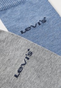 Due paia di calzini: uno blu chiaro e uno grigio, entrambi con il logo Levi's ricamato in contrasto con cuciture navy. Il materiale sembra essere a maglia.