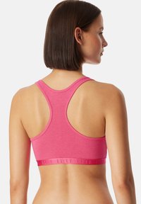 Rosa sport-bh med racerback-design, gjord av mjukt, elastiskt material. Funktioner en elastisk rem med varumärkeslogotypen längst ner.