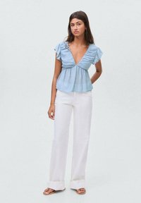 Light blue blouse with a deep V-neck, ruffled short sleeves, and a relaxed fit, paired with white wide-leg pants and casual sandals.
