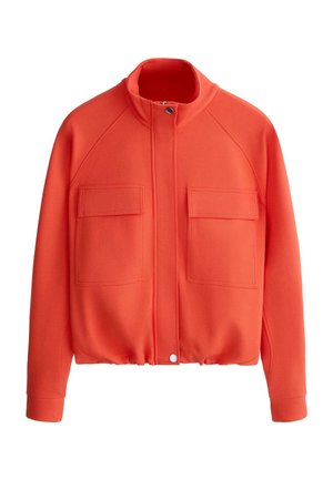 Narancssárga hosszú ujjú dzseki álló gallérral, elöl cipzárral és patenttal, két nagy mellzsebbel fedővel, és elasztikus szegéllyel.