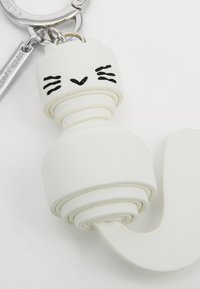 White cat-shaped keychain made from textured synthetic material, featuring a coiled design and black facial details. Silver metal hardware included.