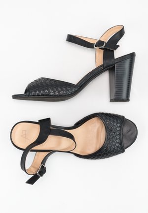 Sorte højhælede sandaler med vævet fronttekstur, åben tå, justerbar ankelrem og mønstret blokhæl. Beige indersål.