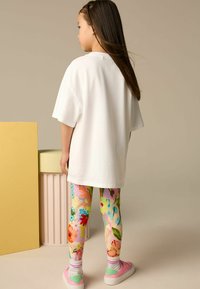 Biała, oversize'owa koszulka, kolorowe legginsy w kwiaty, różowe buty z brokatowymi akcentami oraz paskowane skarpetki. Miękka faktura i żywe wzory.