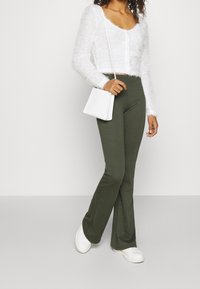 Vitt kortärmat tröja med fluffig textur, olivgröna tajta byxor och vit handväska. Vita skor fulländar outfiten.