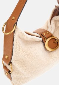 Sac à main en tissu sherpa beige avec des anses en cuir marron et des détails à boucle circulaire et anneau dorés.