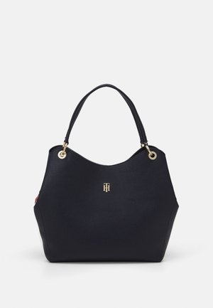 Duża czarna torba typu tote z dwoma uchwytami, złotymi elementami i małym złotym logo Tommy Hilfiger z przodu, na jednolitym tle.