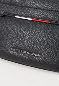 Black textured leather wallet with a silver logo "TOMMY HILFIGER" embossed. Features a tricolor accent in red, white, and blue on the top.