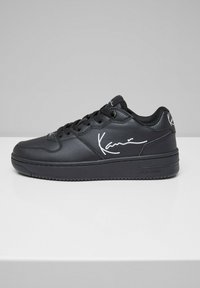 Schwarze Sport sneakers aus strukturiertem Leder, mit gepolstertem Kragen, Schnürverschluss und weißem Markenzeichen an der Seite.