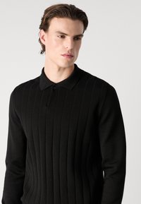Pulover negru tricotat cu dungi verticale, guler cu detaliu din nasture și mâneci lungi, evidențiind o textură netedă și un design ajustat.