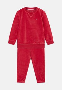Rød velour treningsdrakt med langermet genser med ribbestrikkede mansjetter og matchende bukser. Merkevarelogo på brystet.